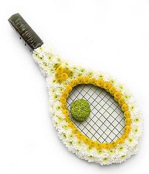 Tennis racket-shaped funeral tribute made with white and yellow sprayed chrysanthemums and a green leaf handle, measuring approximately 60cm x 30cm.
