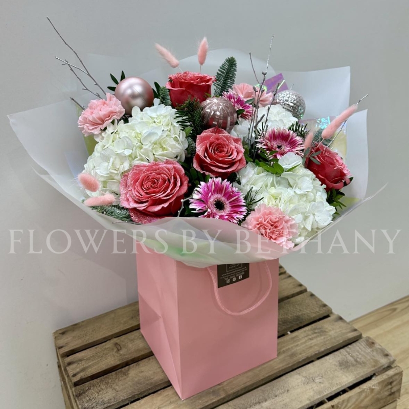 Pink Christmas bouquet with snowy glitter roses, white hydrangea, silver birch, seasonal pink florals and pink baubles, wrapped in iridescent cellophane.